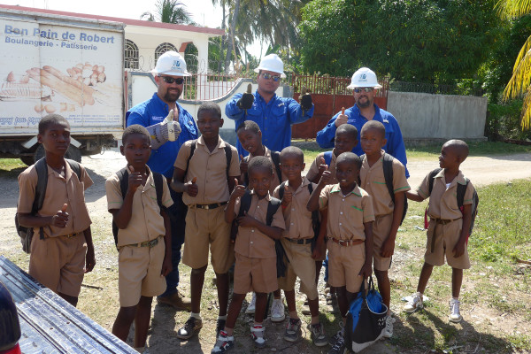 Andy Ridge, Mark Moreno, Marshall Verette from Pedernales Electric Cooperative in Texas pose with school children in Coteaux, Haiti. (Photo courtesy of NRECA International)