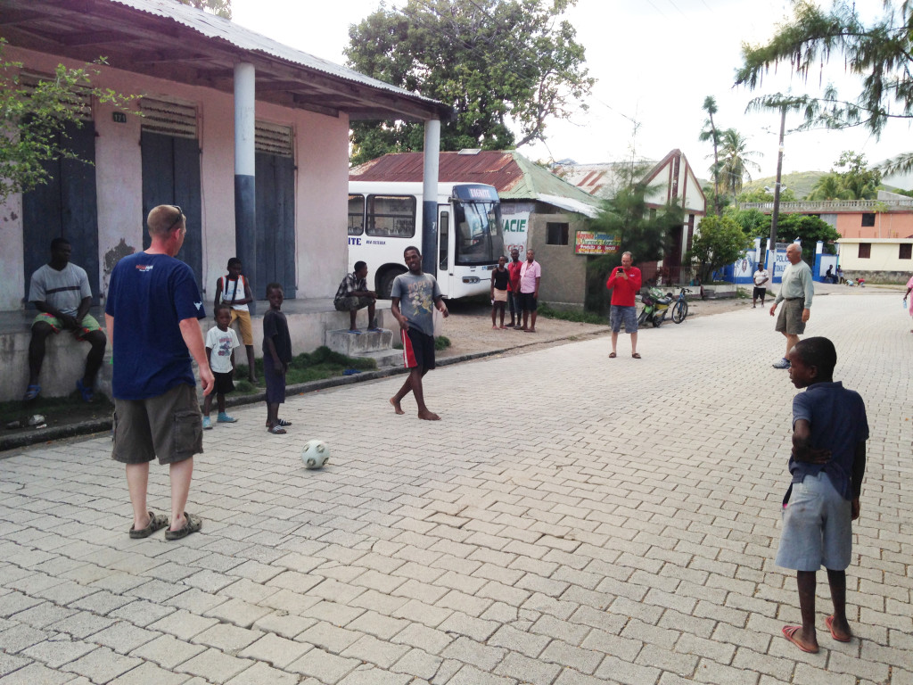Chad Denney (in blue shirt), Tommy Sullivan (red shirt) and Vince Heuser (green shirt) bat around a soccer ball with Haitian youngsters. (Photo By: Zuraidah Hoffman)